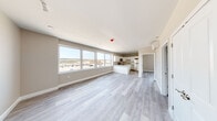 This single-floor unit showcases a clean, contemporary design with a neutral color palette and light wood-style vinyl flooring throughout. The open-concept living and kitchen area is one of the space's most defining features, anchored by a row of large windows along one wall that flood the interior with natural light and offer elevated views of the surrounding area.

The kitchen is thoughtfully appointed with white shaker-style cabinetry, granite-look countertops, and a full suite of stainless steel appliances, including a range, microwave, dishwasher, and refrigerator. A central kitchen island provides additional workspace and helps define the transition between the kitchen and living area. A wall-mounted mini-split HVAC unit ensures efficient climate control throughout the main living space.

The bedroom is a well-proportioned room featuring the same light flooring, neutral wall tones, and a double-door closet offering ample storage. Doors throughout the unit are white-paneled, complementing the overall bright aesthetic.

The layout, as seen in the overhead 3D scan, is efficiently organized with clear distinctions between living, kitchen, and sleeping areas, making the space functional and easy to navigate. Overall, the unit presents a modern, move-in-ready environment with quality finishes and abundant natural light.