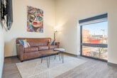 Located at 323 E Wilson St in Madison, WI, this efficiently designed one-bedroom, one-bathroom unit offers a thoughtfully arranged single-floor layout that maximizes every square foot. The open-concept living and kitchen area sets a modern tone, with soaring ceilings that lend an airy sense of volume. Exposed ductwork adds an industrial edge, while light hardwood-style flooring flows throughout the main living space.

The kitchen is well-appointed with navy cabinetry, light stone countertops, a classic white subway tile backsplash, open shelving, and a full suite of stainless steel appliances including a range, dishwasher, and refrigerator. The adjoining living area is bright and welcoming, offering ample wall space for artwork and a comfortable, functional layout.

The bedroom features warm taupe walls and elevated ceilings, creating a cozy yet spacious atmosphere. A sliding barn door adds a stylish, space-conscious touch to the unit's corridor, which also features bold matte black doors with modern hardware.

The bathroom is finished with large-format dark marble-look tile flooring, a wood-toned vanity with under-mount sink, and a glass-enclosed walk-in shower, combining clean lines with warm materials for a polished, contemporary feel.