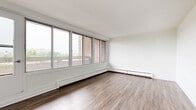 Located at Woodridge Crescent in Ottawa, this 2-bedroom, 1-bathroom unit offers a thoughtfully organized single-floor layout with clean, modern finishes throughout. The living room is a standout space, featuring a expansive bank of large windows that flood the room with natural light and provide open views of the surrounding neighbourhood. Warm laminate hardwood flooring runs throughout the living areas and bedrooms, lending a cohesive and inviting feel to the space. The kitchen is efficiently designed with crisp white cabinetry, dark countertops, a subway tile backsplash, and large-format light grey tile flooring. A stainless steel electric range and ample upper and lower cabinet storage make this a fully functional cooking space. The primary bedroom is generously sized, featuring wide windows with outdoor views and baseboard heating. The second bedroom includes a built-in sliding door closet and matching laminate flooring, offering practical storage solutions. The bathroom is finished with large-format neutral tiles, a soaking tub with a tiled surround, and white cabinetry. Hallways connect each area efficiently, completing this clean and functional residential unit.