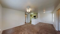 This single-floor residence offers a functional and straightforward layout connecting the main living spaces efficiently. The living room is a generously sized, open area covered in wall-to-wall carpet and illuminated by a ceiling fan with integrated lighting. It flows directly toward the kitchen, which is separated by a white peninsula counter — a practical divide that maintains an open feel between the two spaces. The kitchen is equipped with light wood cabinetry, white countertops, a coil electric range, an over-the-range microwave, and a full-size refrigerator. Hardwood-look flooring runs through the kitchen area, contrasting the carpeted living spaces.

The bedrooms continue the carpeted flooring and are each fitted with ceiling fans. One bedroom features a large sliding glass door with vertical blinds alongside a window overlooking a green outdoor area, allowing for abundant natural light. A second bedroom includes a walk-in closet and a side window. The bathroom is finished with wood-look plank flooring, a full tub/shower combination, a toilet, and a vanity with light wood cabinetry above. Overall, the unit presents a clean, practical interior with a neutral color palette throughout.