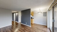Located in Seattle's Meridian neighborhood, this efficiently designed unit offers a thoughtful layout across a single floor. The open-concept main area seamlessly combines the living room, dining space, and kitchen, creating a versatile and connected environment. Rich, dark wood-look flooring runs throughout, complementing the two-tone wall palette of cool gray and light neutral tones. A textured ceiling adds depth to the interior.

The kitchen features warm honey-toned cabinetry with ample upper and lower storage, dark countertops, and black appliances including a range, overhead microwave, and refrigerator. A pendant light fixture adds a finishing touch above the dining area. A dedicated pantry provides additional storage convenience.

The living area benefits from abundant natural light streaming through large sliding glass doors that open onto a private balcony, offering views of surrounding greenery. A dedicated closet and a full bathroom complete the unit. The bathroom is finished with wood-look flooring, white fixtures, a bathtub, and accessibility grab bars. Baseboard heating is present throughout. The overall ambiance is clean, modern, and functional, making efficient use of every square foot.