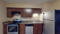 Located at 2233 Courtside Dr in Columbus, Ohio, this single-floor unit offers a practical and well-organized layout. The kitchen is equipped with rich, dark wood cabinetry, dark granite-style countertops, and a full suite of stainless steel appliances, including an electric range, dishwasher, and refrigerator, all set over wood-look tile flooring. The living area is generously sized, featuring wall-to-wall carpet, a large sliding window that invites natural light and outdoor views, a wall-mounted air conditioning unit, and a baseboard heating system. An adjacent room with wood-look laminate flooring offers flexibility as a dining area or den, also benefiting from a window and baseboard heat. The bedrooms are carpeted and feature windows with blinds for natural light and privacy, along with built-in closets with hanging rods for ample storage. The full bathroom includes a tub-shower combination with a curved curtain rod, wood-look flooring, and a clean white vanity. Textured ceilings are consistent throughout, and the warm neutral wall tones create a cohesive, understated aesthetic across all rooms.