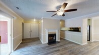 Located at 3278 Colony Ct in Greenville, NC, this single-floor unit offers a well-designed layout with consistent wood-style flooring running throughout. The open living area serves as the heart of the home, highlighted by a classically framed fireplace with a tile surround and white mantel, crown molding, a chair rail, and a ceiling fan overhead. A textured ceiling adds character to the space. Sliding glass doors lead to a private balcony, inviting natural light into the living room. The kitchen is positioned adjacent to the living area in an open-concept arrangement, featuring dark cabinetry, dark countertops, a stainless steel refrigerator, and a built-in oven. The bedrooms are comfortably sized with neutral warm-toned walls, wood-style flooring, and ample natural light provided by windows with blinds. One bedroom includes direct access to a bathroom, offering added convenience. Throughout the unit, clean white baseboards and trim provide a crisp contrast to the warm beige walls, creating a cohesive and welcoming ambiance. The overall design is practical and move-in ready, making this a comfortable and functional space.