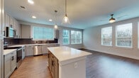 This single-floor residence showcases a thoughtfully designed open-concept layout that connects the kitchen and living areas seamlessly. The kitchen is a standout feature, equipped with shaker-style gray cabinetry accented by matte black hardware, crisp white quartz countertops, a gray subway tile backsplash, and a full suite of stainless steel appliances. A central island with pendant lighting overhead adds both workspace and visual appeal, while recessed lighting and multiple windows ensure the area remains bright and welcoming.

The living space extends naturally from the kitchen, featuring durable wood-look flooring and a ceiling fan, with large windows that invite abundant natural light. Bedrooms are carpeted for comfort, each featuring neutral tones and windows with views of the surrounding area. The primary bedroom connects directly to a private bathroom featuring a glass-enclosed walk-in shower with white subway tile, built-in bench, and matte black fixtures. A secondary full bathroom mirrors the same modern aesthetic, with a gray vanity, black-framed mirror, and wood-look flooring. Throughout the space, clean lines, neutral color palettes, and consistent hardware choices create a cohesive, contemporary atmosphere.
