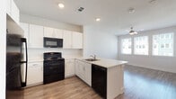 This single-floor unit offers a thoughtfully designed open-concept layout that seamlessly connects the kitchen and living area, creating a spacious and airy feel. The kitchen is a standout feature, equipped with crisp white cabinetry offering generous storage, a peninsula with a light-toned countertop that doubles as a breakfast bar, and a full suite of black appliances including a gas range, over-the-range microwave, dishwasher, and refrigerator. Recessed lighting and a ceiling fan ensure the space remains well-lit and comfortable throughout the day. Wood-look plank flooring extends consistently across the main living areas, adding warmth and visual continuity to the home. The living area benefits from large windows fitted with horizontal blinds, allowing for ample natural light and views of the surrounding neighborhood. A dedicated bedroom provides a quiet retreat, also featuring a ceiling fan, wood-look flooring, and a bright window that fills the room with natural light. The bathroom is finished in a clean, all-white aesthetic, complete with a combined tub and shower enclosure, a single-sink vanity with white cabinetry, and matching wood-look flooring. The overall ambiance of the space is modern, clean, and functional.