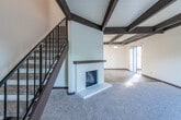 This two-story space is defined by a distinctive architectural character rooted in its bold, dark-stained exposed wood beam ceilings, which run throughout the main living areas and lend a warm, structural aesthetic to the interiors. The main living room is a standout feature, offering generous proportions with a white-surround wood-burning fireplace as its focal point. Carpet flooring extends across the living area, while a sliding glass door provides direct access to an outdoor patio and fills the room with natural light. A staircase with metal balusters connects to the upper level.

A separate room with the same exposed beam ceiling and hardwood-style flooring offers additional living or dining space, also with a sliding glass door leading outside. The kitchen is laid out efficiently with white cabinetry, dark granite-look countertops, and hardwood-style flooring, and is equipped with a range, dishwasher, and sink.

The bedrooms are carpeted and well-sized, each featuring sliding closets with built-in shelving and windows that invite natural light. Bathrooms include a full bath with a tub-shower combination and a vanity, as well as an additional bath with a glass-door shower enclosure.