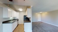 This single-floor unit offers a clean, functional layout with thoughtful finishes throughout. The kitchen is designed as a galley-style space, featuring white shaker cabinetry with brushed nickel hardware, dark quartz countertops, a stainless steel sink, and black appliances including a refrigerator, electric range, and dishwasher. Hardwood-style flooring runs through the kitchen, transitioning seamlessly into the open living area. The living and dining area is generously sized, finished with plush carpet and crown molding along the ceiling. A textured ceiling and ceiling fan add character to the space, while a large sliding glass door leads to a private balcony, filling the room with natural light and offering outdoor views. The bedroom is a comfortable, carpeted retreat with neutral-toned walls and a textured ceiling, providing a calm and restful atmosphere. The bathroom is straightforward and clean, featuring a full tub-and-shower combination with a curved curtain rod and brushed nickel fixtures alongside a standard toilet. Throughout the unit, neutral wall tones, white trim, and consistent flooring choices create a cohesive and move-in-ready aesthetic.