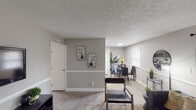 This single-floor residence offers a thoughtfully designed layout that seamlessly connects its living, dining, and kitchen areas. The living room is anchored by a dark sofa accented with warm throw pillows, light wood-style flooring, and floor-to-ceiling green curtains framing a sliding glass door that invites natural light. Wainscoting detail along the lower walls adds a refined architectural touch throughout the common areas.

The adjacent dining area accommodates a glass-top table with modern chairs, positioned near the kitchen for effortless flow. The kitchen features rich, dark-toned shaker-style cabinetry paired with white countertops and a full suite of stainless steel appliances, including a refrigerator, range, microwave, and dishwasher.

The primary bedroom showcases a bold navy accent wall, light wood flooring, and a bright window with blinds, creating a calm and restful atmosphere. The second bedroom offers a neutral palette with floating display shelves, a window with natural light, and a closet, making it a versatile and comfortable space.

The full bathroom includes a shower-tub combination with white tile surround, a single vanity with ample counter space, and textured ceiling detail consistent throughout the home. Light wood-style flooring ties all rooms together cohesively.