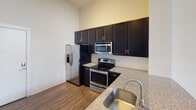 Located at 215 S Irwin Ave in Charlotte, NC, this single-floor residence offers a well-designed layout with modern finishes throughout. The kitchen is a standout feature, outfitted with rich dark cabinetry, granite-style countertops, a tile backsplash, and a full suite of stainless steel appliances including a refrigerator with ice maker, electric range, and built-in microwave. A deep stainless steel sink with a gooseneck faucet completes the functional workspace.

The living and dining area impresses with soaring ceilings that amplify the sense of space, complemented by rich dark hardwood-style flooring that runs throughout. A large floor-to-ceiling window arrangement and a glass sliding door flood the area with natural light and provide views of the surrounding greenery, while a pendant light fixture adds a decorative touch overhead.

The bathroom is finished with consistent dark cabinetry and granite-style countertops, featuring an undermount sink, a large frameless mirror with a modern vanity light bar, and a full tub-shower combination with tile surround and brushed nickel fixtures. Neutral tile flooring ties the room together.

Overall, the space presents a cohesive, contemporary aesthetic with a neutral color palette, quality finishes, and a bright, open atmosphere suited for comfortable urban living in uptown Charlotte.