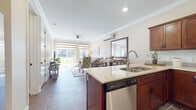 This single-floor residence offers a thoughtfully designed open-concept layout that seamlessly connects the kitchen, dining, and living areas. The kitchen is outfitted with rich cherry wood cabinetry, granite countertops, stainless steel appliances including a range, microwave, and dishwasher, and a central island with bar seating. Wood-look tile flooring and crown molding add a polished, cohesive feel throughout the main living spaces. The dining area comfortably accommodates a full table and flows effortlessly into the living room, which features a ceiling fan, a wall-mounted mini-split system, and large sliding glass doors that invite abundant natural light and outdoor views. Two bedrooms provide comfortable retreats, each fitted with roller shades for adjustable light control and their own mini-split climate units. The bathrooms continue the wood-look tile aesthetic; one includes a full tub-shower combination with tiled surround, while a separate water closet offers added privacy. Neutral wall tones and warm finishes are consistent throughout, creating a calm and inviting ambiance. The space is practical, stylish, and well-suited for comfortable day-to-day living.