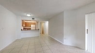 This single-floor residence offers a practical and functional layout throughout. The living area is generously proportioned, finished with light-toned ceramic tile flooring and neutral white walls that create a bright, open atmosphere. A textured ceiling runs throughout the main living spaces, adding subtle visual character. Large sliding glass doors fitted with vertical blinds allow natural light to fill the room while providing outdoor access.

The kitchen is positioned adjacent to the living area and features a pass-through counter that maintains an open connection between the two spaces. Warm honey-toned wood cabinetry lines the walls, complemented by dark laminate countertops and a stainless steel single-basin sink. White appliances, including a coil-burner range and a full-sized refrigerator, are included. Track lighting illuminates the kitchen workspace effectively.

The bedrooms are carpeted and share a consistent design, each equipped with a ceiling fan and light fixture, vertical-blind-covered sliding doors, and textured ceilings. The bathroom includes a wood-toned vanity with an integrated sink, a well-lit mirror, and clean, simple finishes throughout.