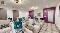 Located at 152 Market St Media in Pittsboro, NC, this single-floor living room is a thoughtfully designed communal screening and lounge space. The room is arranged in a theater-style layout, with rows of cream-upholstered reclining chairs dressed with teal throw blankets and decorative floral pillows, providing a cozy and inviting atmosphere for group gatherings. A plaid area rug anchors the seating arrangement and adds visual texture to the space.

The design is anchored by a bold plum-colored accent wall featuring elegant raised panel detailing, which frames a frosted-glass-panel door and serves as a dramatic focal point. Matching plum-painted cabinetry lines one wall, offering built-in storage and countertop surface space. A wall-mounted flat-screen television is positioned for optimal viewing from all seating areas, supported by in-wall speakers for enhanced audio quality.

Lighting is a blend of recessed ceiling lights and a stylish brass multi-globe flush-mount fixture that adds a warm, refined glow. A window along one wall allows natural light to filter into the space, brightening the neutral cream walls. Subtle gold accent tables are interspersed among the seating. The overall ambiance is polished yet comfortable, blending residential warmth with the functionality of a private screening room.
