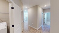 Located at 551-303 Snowmass Loop in Garner, NC, this well-appointed single-story home showcases a clean, modern design with a neutral color palette and quality finishes throughout. The open-concept kitchen serves as the heart of the home, featuring crisp white shaker cabinets extending to the ceiling, a herringbone-patterned subway tile backsplash, light quartz countertops, and a large central island with pendant lighting and an undermount sink. Stainless steel appliances, including a range, microwave, and refrigerator, complete the space. Light luxury vinyl plank flooring flows throughout the main living and kitchen areas, lending a warm, cohesive feel. The primary bedroom is highlighted by a tray ceiling with a ceiling fan and natural light from a large window, complemented by plush carpet flooring. An en-suite primary bathroom offers a dual-sink vanity with white cabinetry, quartz counters, and access to a walk-in closet with built-in shelving. Additional bedrooms also feature soft carpet and ample space. A secondary bathroom mirrors the same refined aesthetic with a single-sink vanity and LVP flooring. A dedicated laundry room houses a full-size washer and dryer with overhead wire shelving. Recessed lighting and matte black hardware details are consistent throughout, adding a contemporary touch.