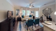 Located at 110 Town Loop in Mooresville, NC, this single-floor residence offers a thoughtfully designed layout with a cohesive, contemporary aesthetic throughout. The open-concept living and dining area serves as the heart of the home, featuring rich hardwood-style flooring, crown molding, and ceiling fans that contribute to a polished, comfortable atmosphere. Multiple windows allow natural light to flow freely, with views of surrounding greenery enhancing the inviting ambiance.

The living room provides generous space for seating and entertainment, while the adjacent dining area accommodates a full dining set with ease. The kitchen is a standout feature, boasting granite countertops, dark espresso cabinetry, stainless steel appliances, a tile backsplash, and a breakfast bar with pendant lighting—ideal for both casual meals and entertaining.

The bedrooms are carpeted for comfort, with the primary bedroom featuring crown molding, a ceiling fan, and access to a well-sized walk-in closet. Each bathroom is finished with wood-look flooring, a soaking tub-shower combination with tile surround, and dark vanity cabinetry paired with light countertops, creating a clean, modern finish throughout.