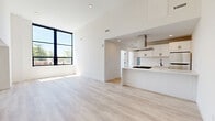 This thoughtfully designed 2-bedroom, 2-bathroom residence in West Haven, Connecticut offers a clean, modern aesthetic throughout its well-appointed single floor. The open-concept living and kitchen area is anchored by soaring ceilings and a striking large black-framed window that floods the space with natural light and frames views of the surrounding neighborhood's mature trees and streetscape. Light-toned hardwood flooring runs seamlessly throughout, enhancing the bright, airy atmosphere.

The kitchen is a standout feature, showcasing white shaker cabinetry with matte black hardware, a quartz waterfall peninsula with an integrated gas cooktop, stainless steel appliances including a gas range and refrigerator, and a stainless steel island range hood. A matte black faucet adds a refined contrast to the clean white surfaces.

Both bedrooms are bathed in natural light, with large black-framed windows offering neighborhood views. The bathrooms are finished with neutral large-format tile, a walk-in shower with a built-in niche, a white vanity with a quartz countertop, and an illuminated round mirror. Additional highlights include two closets, a dedicated laundry area, and a welcoming entrance hallway.