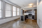 Located at 1118 McGee St in the heart of Kansas City, MO, this modern single-floor urban residence combines contemporary design with functional living. The open-concept kitchen serves as a central highlight, featuring dark wood cabinetry, a white quartz peninsula with a double undermount sink, stainless steel appliances including a range, microwave, and refrigerator, and stylish pendant lighting overhead. Large windows frame views of the surrounding downtown cityscape, flooding the space with natural light. Polished terrazzo floors run throughout the main living and kitchen areas, adding a distinctive and durable finish. The bedroom offers plush carpeting underfoot, a generous walk-in closet, and a narrow clerestory window that allows in additional natural light while maintaining privacy. The bathroom is well-appointed with large-format gray tile surrounding the tub and shower, a sleek floating vanity, a pop of color from an accent wall, and terrazzo flooring that ties back to the rest of the unit. The overall ambiance is clean, contemporary, and urban, making this space well-suited for those seeking a modern lifestyle in the heart of Kansas City.