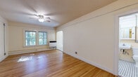 Located in Portland's lively Mississippi Avenue corridor, Unit 202 at 2631 N Mississippi Ave is a charming residence that showcases the character and craftsmanship of a classic Portland building. The living area is bright and welcoming, featuring gleaming hardwood floors that run throughout, large multi-pane windows that invite generous natural light and leafy outdoor views, and a ceiling fan overhead. A distinctive arched doorway connects the living space to the rest of the unit, adding an elegant architectural touch that speaks to the building's vintage roots. The kitchen retains its period charm with white painted cabinetry featuring traditional hardware, a classic black-and-white hexagonal mosaic tile floor, a stainless steel sink, and ample counter and storage space. A compact, open shelving unit adds additional utility. The bathroom echoes the kitchen's retro aesthetic with matching hexagonal tile flooring, a pedestal sink, a medicine cabinet with mirror, and a full soaking tub with shower. A warm entry area with a distinctive glass-paned interior door, a ceiling fan, and an open closet provides a welcoming transition into the home. Throughout, neutral warm tones and preserved original details create an ambiance that is both cozy and full of timeless Portland character.