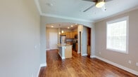 This single-floor residence at Olde Towne Apartments offers a thoughtfully designed open-concept layout that seamlessly connects the living and kitchen areas. Rich hardwood-style flooring runs throughout, lending warmth and continuity to the space. A ceiling fan in the living area provides both comfort and a finishing architectural touch, while crown molding along the ceilings adds a refined, classic detail.

The kitchen is accessed through an elegant arched passageway, creating a graceful transition between spaces. It features warm honey-toned cabinetry, granite countertops, and a suite of stainless steel appliances including a refrigerator, range, and microwave. A kitchen island with a built-in sink serves as both a functional workspace and a casual dining or gathering spot, illuminated by stylish pendant lighting overhead. Recessed lighting throughout the kitchen ensures the area is well-lit and practical.

Adjacent to the kitchen, a built-in shelving unit provides convenient display and storage space, adding character and utility to the layout. The overall color palette of soft grays and warm wood tones creates a welcoming and cohesive ambiance throughout the home, making it a comfortable and functional living environment.