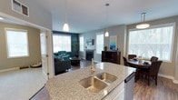 This single-floor, 2-bedroom, 2-bathroom home is designed with an open-concept layout that seamlessly connects the kitchen, dining, and living areas, creating a bright and functional environment. The kitchen serves as the centerpiece of the space, featuring a large granite-topped island with a double undermount sink, pendant lighting overhead, and white cabinetry. The island naturally anchors the layout, offering both prep space and a visual transition into the adjoining areas.

The living room is highlighted by a fireplace flanked by multiple windows that invite abundant natural light, giving the space a warm and welcoming ambiance. Hardwood-style flooring runs throughout, providing a cohesive and polished look. The dining area sits adjacent to the kitchen, benefiting from additional window exposure and easy access to the main living zone.

The teal accent wall in the living area adds a bold design touch, complementing the neutral gray tones used throughout. The overall layout is well-proportioned, offering comfortable flow between spaces. With two full bathrooms and two bedrooms, this home provides practical functionality alongside its modern aesthetic appeal.