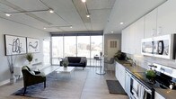 This contemporary one-bedroom, one-bathroom residence offers a thoughtfully designed open-concept layout that seamlessly connects the living, dining, and kitchen areas into a cohesive and functional living space. Exposed concrete ceilings with industrial-style track lighting lend a distinctive urban character, while wide-plank light hardwood flooring grounds the interior with warmth and continuity throughout.

The living area is anchored by expansive floor-to-ceiling windows that flood the space with natural light and frame impressive panoramic views of the surrounding city skyline, creating a striking visual backdrop for everyday living. The open kitchen features clean white cabinetry, a subway tile backsplash, modern stainless steel appliances, and a sleek countertop with an undermount sink — delivering both style and practicality. A bistro-style dining table with bar seating provides a casual yet elegant spot for meals.

The overall ambiance is modern and airy, with an industrial-chic aesthetic defined by the interplay of raw concrete, crisp white finishes, and abundant natural light. The layout makes efficient use of every square foot, offering a comfortable and well-appointed urban living experience with city views as a defining feature.