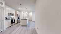 This single-floor, 2-bedroom, 2-bathroom residence offers a clean, contemporary design with a neutral color palette throughout. The open-concept kitchen is a standout feature, showcasing light wood cabinetry, a subway tile backsplash, stainless steel appliances, and a central island with granite countertops topped by stylish pendant lighting. A built-in desk nook adds a practical touch to the kitchen area. Light wood-style luxury vinyl plank flooring flows through the main living areas, complementing the bright, airy atmosphere created by recessed lighting and large windows with natural light throughout. The living room benefits from large windows overlooking greenery, enhancing the sense of openness. Both bedrooms are carpeted and feature ceiling fans and windows with blinds. The primary bedroom is a well-sized retreat, connected to a private bathroom with a dual-sink vanity featuring granite countertops and light wood cabinetry. A dedicated closet offers multi-tiered shelving and hanging rods for generous storage. The second bedroom is similarly comfortable, sharing access to the second full bathroom. The overall ambiance is modern, clean, and move-in ready, with cohesive finishes tying every room together seamlessly.