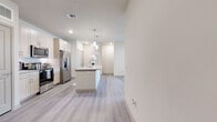 This single-floor, 2-bedroom, 2-bathroom residence offers a clean, contemporary design with a neutral color palette throughout. The open-concept kitchen is a standout feature, showcasing light wood cabinetry, a subway tile backsplash, stainless steel appliances, and a central island with granite countertops topped by stylish pendant lighting. A built-in desk nook adds a practical touch to the kitchen area. Light wood-style luxury vinyl plank flooring flows through the main living areas, complementing the bright, airy atmosphere created by recessed lighting and large windows with natural light throughout. The living room benefits from large windows overlooking greenery, enhancing the sense of openness. Both bedrooms are carpeted and feature ceiling fans and windows with blinds. The primary bedroom is a well-sized retreat, connected to a private bathroom with a dual-sink vanity featuring granite countertops and light wood cabinetry. A dedicated closet offers multi-tiered shelving and hanging rods for generous storage. The second bedroom is similarly comfortable, sharing access to the second full bathroom. The overall ambiance is modern, clean, and move-in ready, with cohesive finishes tying every room together seamlessly.