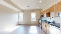 This single-floor unit offers a clean, contemporary design with a thoughtfully laid-out open-concept floor plan. The combined kitchen and living area is bathed in natural light streaming through multiple windows, which frame views of the surrounding urban streetscape. Light-toned hardwood flooring runs throughout the main living spaces, lending warmth and visual continuity to the interior.

The kitchen is a standout feature, equipped with a full suite of stainless steel appliances including a range, over-the-range microwave, dishwasher, and refrigerator. Warm honey-toned wood cabinetry with black hardware lines the walls, complemented by dark countertops and a light blue subway tile backsplash that adds a subtle pop of color. A deep undermount sink and ample upper and lower cabinet storage round out this functional and stylish kitchen.

The bedroom is generously proportioned, featuring neutral walls, light hardwood flooring, a window with an urban view, and a closet for convenient storage.

The bathroom is finished with large-format tile flooring, a rich dark-wood vanity with a white countertop and undermount sink, a framed mirror, and contemporary wall-mounted lighting, creating a polished and practical space.

Recessed lighting throughout and neutral wall tones contribute to the clean, modern ambiance of this well-designed unit.