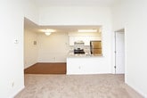 This single-floor residence offers a well-organized layout designed for comfortable everyday living. The open-plan living and dining area features neutral-toned carpet and connects seamlessly to the kitchen, which is outfitted with white shaker-style cabinetry, granite-look countertops, stainless steel appliances including an electric range and refrigerator, and a peninsula with a sink — all set over warm hardwood-style flooring. The living area is bright and spacious, with a front entry door flanked by a window that allows natural light to fill the room.

The bedrooms are carpeted and generously sized, each featuring large multi-pane windows that offer views of the surrounding residential neighborhood. One bedroom includes a walk-in closet equipped with wire shelving, providing ample storage space.

The full bathroom is clean and functional, featuring white cabinetry with a granite-look vanity countertop, a mirror with overhead lighting, and a full-size tub and shower combination with a curved curtain rod and chrome fixtures. The bathroom floor is finished in hardwood-style material, consistent with the kitchen.

Throughout the residence, the light-colored walls and neutral finishes create a bright, cohesive aesthetic that lends itself well to a variety of interior styles.