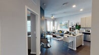 This thoughtfully designed single-floor residence showcases a seamless open-concept layout that connects the kitchen, dining, and living areas into one cohesive and inviting space. Dark hardwood-style flooring runs throughout, anchoring the contemporary aesthetic and providing a striking contrast to the light-toned walls and ceilings fitted with recessed lighting and a ceiling fan.

The kitchen is a standout feature, outfitted with light wood grain cabinetry extending to the ceiling, granite countertops, a full suite of stainless steel appliances, and a central island that doubles as a breakfast bar with seating. Adjacent to the kitchen, a cozy dining nook accommodates a round glass-top table, while the open living area offers generous space for lounging, complete with large windows and a glass door that flood the room with natural light.

The bedroom is a dramatic retreat, highlighted by a deep teal accent wall, bold artwork, and a walk-in closet with built-in shelving. The ensuite bathroom features granite vanity countertops, modern wood-toned cabinetry, and tile flooring. A secondary bedroom area with a wall-mounted television and a neutral grey palette provides additional flexible living space. The overall ambiance is modern, curated, and sophisticated.