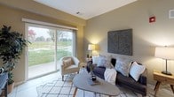 Located at 225 Mt Hope Ave in Rochester, NY, this single-floor residence offers a thoughtfully designed layout with a cohesive, neutral aesthetic throughout. The galley-style kitchen is equipped with light maple cabinetry, stainless steel appliances including a range, microwave, and refrigerator, granite-style countertops, and tile flooring. An in-unit stacked washer and dryer are conveniently accessible from the kitchen area.

The living room is a welcoming space featuring a large sliding glass door that floods the room with natural light and provides direct views of the surrounding green landscape. The warm, neutral wall tones and open layout create a relaxed and inviting atmosphere.

The primary bedroom is generously sized with plush carpeting, a large window overlooking the outdoors, and ample room for furnishings. A secondary bedroom offers the same carpeted comfort and a serene ambiance. An additional flexible room with a window and natural light serves well as a sitting room, office, or den.

The bathroom is finished with large-format stone-look wall tiles in the shower area, tile flooring, a granite-topped vanity, and a mirror — delivering a clean, modern look. Throughout the residence, warm taupe walls, consistent flooring materials, and abundant natural light from multiple windows contribute to a calm and cohesive living environment.