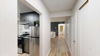 Located at 11405 132 St in Edmonton, AB, this well-appointed one-bedroom, one-bathroom unit offers a thoughtfully designed layout across a single floor. Light wood laminate flooring runs throughout, creating a warm and cohesive feel across all rooms.

The living room features a large window dressed with zebra blinds, a built-in baseboard heater, and a neutral grey and navy accent wall that adds depth and character to the space. An entryway area is accented by a decorative navy sideboard and arched gold-framed mirrors, setting an elegant tone upon entry.

The kitchen is efficiently laid out with dark wood-toned cabinetry, grey stone countertops, a tile backsplash, and stainless steel appliances including a refrigerator and electric range with a hood fan. A dedicated dining nook adjacent to the kitchen comfortably accommodates a full dining set beneath a bright window.

The bedroom is a standout feature, showcasing a striking slate-blue panel accent wall, a large zebra-blind window, and a ceiling light fixture, offering a cozy and refined retreat.

The bathroom is finished with marble-look tile surrounds in the combined tub and shower, complemented by chrome fixtures for a clean, polished look.

Hallways connect the rooms efficiently, and the overall interior palette of soft greys, warm wood, and blue accents lends the space a modern, cohesive aesthetic.