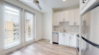 This two-story space showcases a clean, modern design throughout, with a cohesive neutral color palette of crisp whites and warm beige tones that create a bright, airy atmosphere across both levels.

The kitchen is thoughtfully outfitted with white shaker-style cabinetry accented by matte black hardware, light quartz countertops, and a classic tile backsplash. A full suite of stainless steel appliances includes a refrigerator, electric range, over-the-range microwave, and dishwasher. Light wood-style luxury vinyl plank flooring runs through the kitchen and dining area, which benefits from natural light through large windows and a glass door leading to an outdoor balcony. A ceiling fan overhead provides additional comfort.

The bedrooms are carpeted in a warm neutral tone, offering a softer underfoot feel, and feature ceiling fans and ample natural light from generously sized windows. Closet space is accessible directly from the bedrooms.

The bathrooms are finished in a consistent modern style, with white shaker vanity cabinetry, white quartz countertops, backlit mirrors, and wood-style plank flooring. A full bathroom with a walk-in shower and a secondary half-bath provide convenience across the two floors. Overall, the space presents a polished, move-in-ready aesthetic.