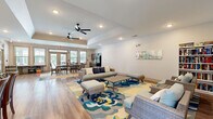 Located at 200 Governors Ct in Cartersville, Georgia, this single-floor community space is thoughtfully designed to accommodate a variety of gathering and leisure activities. The open-plan layout seamlessly connects multiple functional zones, all unified by warm wood-look flooring and a clean, neutral color palette throughout.

The lounge area serves as the centerpiece of the space, featuring comfortable wicker-style seating arranged around a bold floral area rug in shades of blue, yellow, and teal. Ceiling fans overhead and recessed lighting contribute to a relaxed, welcoming atmosphere. A built-in bookshelf and decorative wall art add character and a sense of comfort to the lounge.

Adjacent to the lounge, a dining area accommodates seated gatherings with a rectangular white-top table and cushioned chairs. Large windows with blinds line the walls, flooding the interior with natural light and offering views of the surrounding greenery. Glass-paned entry doors provide additional brightness and easy outdoor access.

The kitchenette area is equipped with gray cabinetry, a sink, a full-size refrigerator, and a microwave — providing practical support for events and everyday use. A tray ceiling detail adds architectural interest, while the overall design remains clean, modern, and highly functional — making this a well-rounded community gathering space.