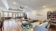 Located at 200 Governors Ct in Cartersville, Georgia, this single-floor community space is thoughtfully designed to accommodate a variety of gathering and leisure activities. The open-plan layout seamlessly connects multiple functional zones, all unified by warm wood-look flooring and a clean, neutral color palette throughout.

The lounge area serves as the centerpiece of the space, featuring comfortable wicker-style seating arranged around a bold floral area rug in shades of blue, yellow, and teal. Ceiling fans overhead and recessed lighting contribute to a relaxed, welcoming atmosphere. A built-in bookshelf and decorative wall art add character and a sense of comfort to the lounge.

Adjacent to the lounge, a dining area accommodates seated gatherings with a rectangular white-top table and cushioned chairs. Large windows with blinds line the walls, flooding the interior with natural light and offering views of the surrounding greenery. Glass-paned entry doors provide additional brightness and easy outdoor access.

The kitchenette area is equipped with gray cabinetry, a sink, a full-size refrigerator, and a microwave — providing practical support for events and everyday use. A tray ceiling detail adds architectural interest, while the overall design remains clean, modern, and highly functional — making this a well-rounded community gathering space.