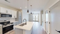 Located at 400 Universal Rd in Southern Pines, NC, this well-designed one-bedroom, one-bathroom residence offers a thoughtful layout with modern finishes throughout. Warm hardwood-style flooring flows consistently across the entire unit, complementing the clean, neutral color palette that creates a bright and inviting atmosphere.

The kitchen serves as a central highlight, anchored by a substantial island with an undermount sink and sleek white quartz countertops. Shaker-style cabinetry in a crisp white-gray finish, paired with matte black hardware, lines the walls and provides generous storage. Stainless steel appliances, including a refrigerator, range, and over-the-range microwave, complete the modern culinary space. Recessed lighting and stylish pendant fixtures illuminate the area effectively.

The living area is open and airy, featuring a ceiling fan and a set of French doors that lead to a private outdoor space, allowing natural light to pour in and offering pleasing exterior views. The bedroom is a comfortable, well-proportioned retreat with a ceiling fan, a large window framing outdoor views, and direct access to a spacious walk-in closet with wire shelving for ample organization.

The bathroom is elegantly appointed with a single-sink vanity topped with white quartz, matte black fixtures, and a glass-enclosed walk-in shower, all set over warm hardwood-style flooring.