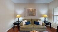This single-floor residence at 809 E Main St in Lexington, SC offers a well-organized layout with a comfortable blend of functional spaces and warm finishes throughout. Rich hardwood flooring flows through the main living areas, creating a cohesive and inviting atmosphere from the moment you enter.

The living room is bright and welcoming, with natural light streaming in through large windows that frame views of surrounding greenery. It connects seamlessly to the dining area, which features a multi-pane window bay and an elegant chandelier overhead, providing a naturally lit setting ideal for everyday meals or entertaining.

The galley-style kitchen is efficiently designed with ample cabinetry, dark countertops, and white appliances, including a range, microwave, and refrigerator. A peninsula counter adds additional workspace, and the kitchen connects directly to the dedicated laundry area, which houses a full-size washer and dryer with overhead wire shelving for storage.

The bedrooms offer a calm retreat, with plush carpeting, neutral toned walls, and windows that let in natural light. The full bathroom features hardwood-style flooring, a tub and shower combination, and a vanity with counter space. Throughout the residence, textured ceilings and clean white trim contribute to a tidy, classic aesthetic suited for comfortable everyday living.