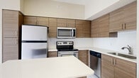 This contemporary 750 square foot apartment in AMLI Dadeland, Miami, offers a thoughtfully designed living space over a single floor. The unit features two bedrooms, including a generously sized primary bedroom of 160 square feet, and one bathroom. The open-concept layout seamlessly integrates the living areas, creating a sense of spaciousness and flow.

The kitchen is a highlight, boasting modern wood-grain cabinetry, sleek stainless steel appliances, and a subway tile backsplash. A central island with seating provides additional counter space and a casual dining area. The light-colored tile flooring in the kitchen transitions smoothly to warm wood-look flooring throughout the rest of the apartment, unifying the space.

Both bedrooms offer ample natural light through large windows, with the primary bedroom showcasing urban views. Built-in closets provide storage solutions. The bathroom features a modern vanity, a tiled shower/tub combination, and continues the apartment's clean, contemporary aesthetic.

Throughout the apartment, neutral wall colors and recessed lighting create a bright, airy ambiance. Ceiling fans in the bedrooms offer additional comfort. The overall design reflects a modern urban lifestyle, balancing functionality with style in this Miami residence.