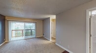 This single-floor residence offers a functional and straightforward layout with a variety of distinct living spaces. The main living area is a generously sized room featuring a combination of wood-style hard flooring and plush carpeting, neutral-toned walls painted in a muted blue-gray, and a ceiling fan with integrated lighting. A sliding glass door fitted with vertical blinds opens directly onto a private balcony, allowing natural light to fill the space and providing outdoor views of surrounding greenery.

Adjacent to the living area, a hallway connects to the remaining rooms. The kitchen is equipped with white appliances, including an electric range and over-the-range microwave, complemented by warm wood cabinetry, granite-style countertops, and tile flooring. A window fitted with horizontal blinds brings in additional natural light.

The bedrooms are carpeted and finished with neutral walls and textured ceilings, offering a quiet and comfortable atmosphere. Each room features windows that provide natural light and ventilation. The bathroom includes a full tub and shower combo with built-in shelving, chrome fixtures, and a clean, all-white finish. Throughout the unit, textured ceilings, white baseboards, and consistent neutral tones contribute to a cohesive and practical interior aesthetic.