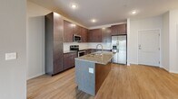 Located at 13650 Marsh View Blvd in Rogers, MN, this single-floor 2-bedroom, 2-bathroom residence offers a thoughtfully designed open-concept layout. The combined kitchen and living area serves as the heart of the home, with light wood-style flooring flowing throughout. The kitchen is a standout feature, showcasing rich dark-wood cabinetry extending to the ceiling, a classic white subway tile backsplash, granite countertops, a center island with a built-in sink, and a full suite of stainless steel appliances including a refrigerator, range, and microwave. The living area is bright and airy, benefiting from natural light and sliding door access to a private balcony. The primary bedroom offers a generous footprint with plush carpeting, and is complemented by a spacious walk-in closet outfitted with wire shelving on multiple levels. The second bedroom features carpet flooring and a large window with exterior views. Both bathrooms are finished with granite-topped dark vanities and wood-look tile flooring, with the primary bath including additional cabinetry for storage. The unit also includes a dedicated laundry room and utility room for added convenience.