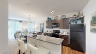 Located at 416 E North Pointe Dr in Salisbury, Maryland, this single-floor residence offers a thoughtfully designed layout with contemporary finishes throughout. The open-concept kitchen is a standout feature, equipped with dark espresso cabinetry, granite countertops, black appliances including a range, microwave, and refrigerator, and a breakfast bar peninsula that flows seamlessly into the dining and living areas. Hardwood-style flooring runs through the kitchen and extends toward the main living spaces, adding warmth and cohesion to the design. The living room is bright and inviting, featuring plush carpeting and a large sliding glass door that floods the room with natural light and provides direct access to a private outdoor balcony with scenic views. Two well-appointed bedrooms feature soft carpeting, ample natural light from generously sized windows, and neutral tones that create a calm, restful atmosphere. The bathroom mirrors the kitchen's design aesthetic with matching dark cabinetry, granite countertops, a wide vanity mirror, and hardwood-style flooring. A dedicated in-unit laundry area with full-size washer and dryer hookups and overhead shelving adds everyday practicality. The overall ambiance is clean, modern, and move-in ready.