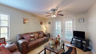 Located at 1936 Shelton Beach Road Ext in Mobile, Alabama, this single-story home offers a practical and comfortable layout across its well-utilized floor plan. The living room serves as a welcoming central space, featuring light tile flooring, a ceiling fan, and French doors that invite natural light and provide outdoor access. The galley-style kitchen is efficiently designed with warm wood cabinetry, dark granite-style countertops, and black appliances including a range, microwave, and refrigerator — offering ample storage and counter space. Adjacent to the kitchen, the dining area accommodates a four-seat dining set beneath a pendant light fixture, creating a defined space for meals. The bedroom is generously sized, outfitted with plush carpet flooring, a ceiling fan with light fixture, large windows that allow natural light, and a closet. The full bathroom features a wood vanity with a granite-style countertop, a single sink, and tile flooring, maintaining the consistent, neutral aesthetic found throughout the home. Overall, the space presents a cohesive, functional design with tile flooring in the main living areas and a neutral color palette that creates a clean, inviting atmosphere throughout.