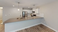 Located at 4301 Breton Rd SE in Grand Rapids, Michigan, this well-appointed single-floor unit offers a clean, modern aesthetic throughout. The open-concept living and dining area is finished with durable wood-look flooring and neutral warm-toned walls, creating a bright and welcoming atmosphere. An elegant chandelier anchors the dining space, which benefits from generous natural light through large windows with blinds. A sliding glass door in the living area leads to an outdoor space, further enhancing the sense of openness. The kitchen is a standout feature, boasting white shaker-style cabinetry, a classic subway tile backsplash, sleek gray quartz countertops, and a full suite of stainless steel appliances including a refrigerator, range, microwave, and dishwasher. Pendant lighting above the kitchen peninsula adds a stylish finishing touch. The bedroom features plush wall-to-wall carpeting, soft gray walls, and a window that allows for natural light, along with a private door for added convenience. The bathroom is finished with wood-look tile flooring and includes a walk-in shower unit and modern brushed nickel fixtures. Overall, the space presents a cohesive, contemporary design that is both functional and visually appealing.