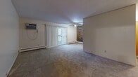 Located at 4285 River St in Willoughby, OH, this single-floor, 2-bedroom, 1-bathroom unit offers a functional and comfortable layout. The living room is the centerpiece of the home, featuring plush carpet flooring, a ceiling fan, a baseboard heating system, and a wall-mounted air conditioning unit. A sliding glass door opens to a private balcony, allowing natural light to fill the space, while a distinctive exposed brick accent wall adds a warm, textural element to the room. The kitchen is positioned adjacent to the living area and includes wood-toned cabinetry. A connecting hallway leads to both bedrooms, each outfitted with carpet flooring, ceiling fans with integrated lighting, baseboard heating, and windows that bring in natural light and outdoor views. Both bedrooms feature warm wood-toned sliding closet doors, providing ample storage. The bathroom is finished with classic white square tile surrounding a full soaking tub and shower combination, accented by a decorative tile border. The overall layout is straightforward and efficient, with warm neutral tones and wood accents throughout creating a cohesive and livable atmosphere.