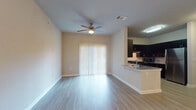 This single-story unit offers a well-designed open-concept layout that seamlessly connects the living and kitchen areas. The living space is finished with light wood-look flooring throughout and features a ceiling fan with integrated lighting. A sliding glass door fitted with vertical blinds allows natural light to fill the room and provides access to the exterior.

The kitchen is a standout feature, showcasing dark espresso cabinetry that extends to the upper walls, providing generous storage. Granite countertops run along the U-shaped layout, complemented by a classic white subway tile backsplash. Stainless steel appliances, including a gas range, microwave, and refrigerator, complete the space. A peninsula with a granite overhang connects the kitchen to the living area, ideal for casual dining or entertaining.

A dedicated room near the entryway offers built-in shelving and a built-in desk, functioning well as a home office or study. The bathroom is cleanly finished, featuring a dark vanity with a granite countertop, a framed mirror, and a combination tub and shower. Wood-look flooring carries consistently through all areas of the unit, contributing to a cohesive, modern aesthetic throughout.