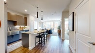 Located on Chester Street in Aurora, Colorado, this well-appointed 2-bedroom, 2-bathroom residence offers a thoughtfully designed single-floor layout with modern finishes throughout. The open-concept kitchen and living area serves as the heart of the home, featuring rich hardwood-style flooring, a granite-topped island with bar seating, two striking black pendant lights, and sleek two-tone cabinetry in walnut and slate blue. The kitchen is further elevated by a stainless steel farmhouse sink, tile backsplash, and under-cabinet lighting. The living room flows naturally from the kitchen and is bathed in natural light from large windows and a glass door that opens to a private balcony with outdoor views. The primary bedroom offers a comfortable footprint with plush carpeting, a ceiling fan, and a window overlooking the neighborhood. Its en-suite bathroom includes a glass-enclosed walk-in shower with full tile surround. The second bedroom features a walk-in closet and ceiling fan. The second bathroom is finished with a granite-topped vanity with an illuminated mirror, gray cabinetry, wood-look flooring, and a tiled tub-shower combination. Together, these spaces create a cohesive, contemporary living environment with quality finishes at every turn.