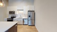 Located at 247 4th St E in downtown Saint Paul, Minnesota, this two-floor space masterfully combines historic industrial character with thoughtfully modern upgrades. The upper level serves as the primary living and working area, anchored by a fully equipped kitchen outfitted with white shaker cabinetry, stainless steel appliances including a French door refrigerator, electric range, built-in microwave, and dishwasher. White quartz countertops and a herringbone-patterned tile backsplash add a refined touch, while light hardwood flooring runs throughout. Soaring ceilings with exposed metal ductwork and large windows flooding the space with natural light and views of surrounding greenery reinforce the loft-like industrial aesthetic. A sleek steel-cable staircase with dark metal railings connects the two levels, adding a striking architectural focal point. Bathrooms on the upper level feature dark wood vanities, large framed mirrors, white quartz counters, and classic black-and-white octagon tile flooring. The lower level retains its original exposed stone and concrete masonry walls—a nod to the building's historic roots—paired with neutral carpet, corrugated metal ceilings, and pendant lighting, creating a versatile, characterful space suitable for a variety of uses.