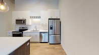 Located at 247 4th St E in downtown Saint Paul, Minnesota, this two-floor space masterfully combines historic industrial character with thoughtfully modern upgrades. The upper level serves as the primary living and working area, anchored by a fully equipped kitchen outfitted with white shaker cabinetry, stainless steel appliances including a French door refrigerator, electric range, built-in microwave, and dishwasher. White quartz countertops and a herringbone-patterned tile backsplash add a refined touch, while light hardwood flooring runs throughout. Soaring ceilings with exposed metal ductwork and large windows flooding the space with natural light and views of surrounding greenery reinforce the loft-like industrial aesthetic. A sleek steel-cable staircase with dark metal railings connects the two levels, adding a striking architectural focal point. Bathrooms on the upper level feature dark wood vanities, large framed mirrors, white quartz counters, and classic black-and-white octagon tile flooring. The lower level retains its original exposed stone and concrete masonry walls—a nod to the building's historic roots—paired with neutral carpet, corrugated metal ceilings, and pendant lighting, creating a versatile, characterful space suitable for a variety of uses.