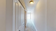This single-floor high-rise unit offers a well-organized layout with a clean, neutral aesthetic throughout. The spacious main living area is finished with plush grey carpeting and warm taupe walls, creating a calm and versatile backdrop. A large sliding glass door leads to a private balcony, flooding the room with natural light and revealing striking panoramic views of the city skyline and what appears to be a body of water in the distance — a standout feature of the space. A secondary room, also carpeted and generously sized, connects seamlessly to the hallway and provides access to additional storage through mirrored sliding closet doors. The hallway runs the length of the unit, finished with the same soft carpeting and illuminated by a warm gold flush-mount ceiling fixture. Textured ceilings carry throughout the space, adding a classic residential character. The bathroom is thoughtfully appointed with a white vanity featuring cabinet storage, a large mirror, a multi-light brushed nickel fixture, and a full tub-shower combination with tiled surround. Rich hardwood flooring in the bathroom provides a warm contrast to the carpeted areas. Overall, the unit presents a functional and comfortable layout with notable views and practical storage solutions.