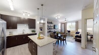 This single-floor residence is designed with a contemporary aesthetic, characterized by a cohesive color palette of warm neutrals, dark espresso cabinetry, and light wood-style flooring throughout the main living areas. The open-concept layout seamlessly connects the kitchen, dining, and living spaces, creating a functional and visually expansive environment.

The kitchen serves as a focal point, featuring rich dark cabinetry that extends to the ceiling, stainless steel appliances including a refrigerator, microwave, and range, and a granite-topped island with bar seating illuminated by pendant lighting. Track lighting above adds additional task illumination. A white tile backsplash provides a clean contrast to the dark cabinetry.

The living area benefits from natural light through large windows and a sliding door, and is equipped with a ceiling fan. Open shelving flanks the wall-mounted television area. The dining space sits comfortably between the kitchen and living room.

Both bedrooms feature plush carpeting, ceiling fans, closets, and windows allowing natural light. The bathrooms echo the kitchen's design language with granite countertops, dark vanity cabinetry, undermount sinks, and large mirrors. One bathroom includes a tiled soaking tub and shower combination.