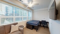 Located at 505 S Fifth St in Champaign, Illinois, Unit 213 is a thoughtfully designed one-bedroom, one-bathroom residence that maximizes its efficient footprint with a clean, modern aesthetic throughout. The open-concept living and kitchen area serves as the heart of the unit, featuring light wood-tone flooring that carries seamlessly through the space. The kitchen is well-appointed with gray shaker-style cabinetry, white quartz countertops, a white subway tile backsplash, and a full suite of stainless steel appliances including a gas range, over-the-range microwave, dishwasher, and refrigerator. A built-in bistro-style table with seating provides a convenient dining area just off the kitchen. The living area offers a comfortable, naturally lit space with a window overlooking the surroundings. The bedroom is a private, cozy retreat featuring a window with blinds for natural light and climate control. The bathroom is finished in a crisp, contemporary style with warm wood-tone flooring, white walls, black hardware accents, and a glass-enclosed shower stall. Recessed lighting throughout adds a clean, modern touch, making this unit a functional and stylish option in the heart of Champaign.